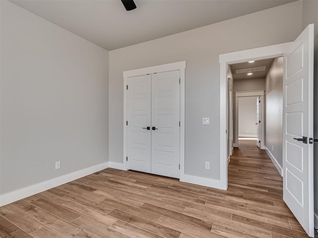 unfurnished bedroom featuring ceiling fan, a closet, and light wood-type flooring