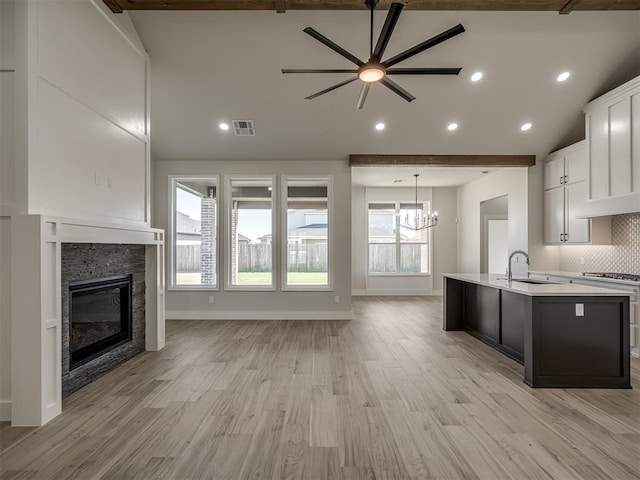 kitchen with sink, stainless steel gas range oven, white cabinetry, a fireplace, and a kitchen island with sink