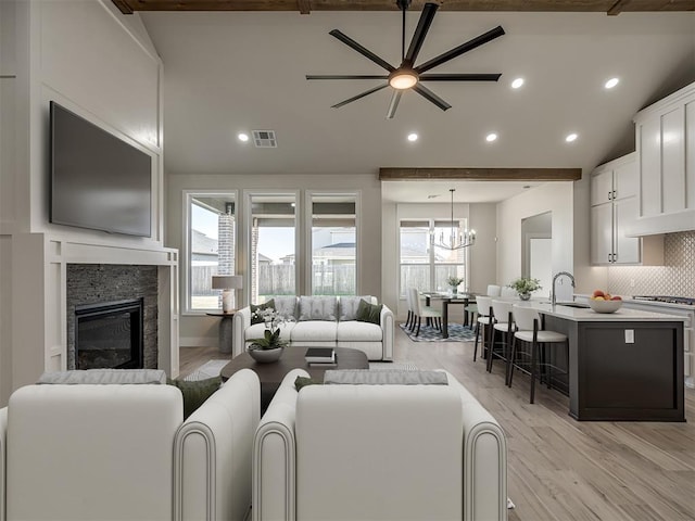 living room with a notable chandelier, a fireplace, light hardwood / wood-style floors, and vaulted ceiling