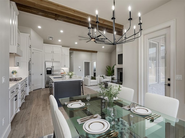 dining room with beamed ceiling, sink, and light hardwood / wood-style flooring