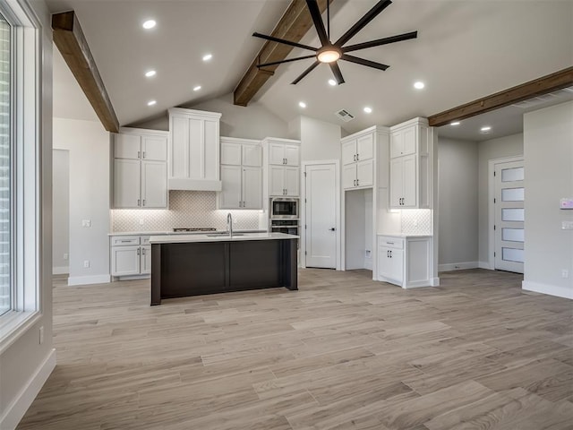 kitchen with white cabinetry, appliances with stainless steel finishes, a kitchen island with sink, and lofted ceiling with beams