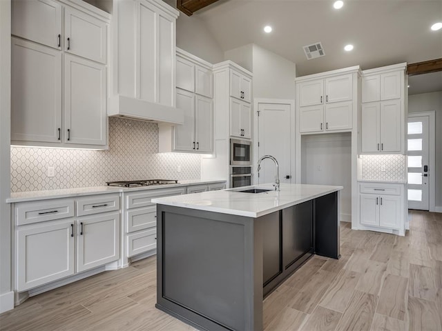 kitchen with white cabinetry, an island with sink, backsplash, stainless steel appliances, and light hardwood / wood-style flooring