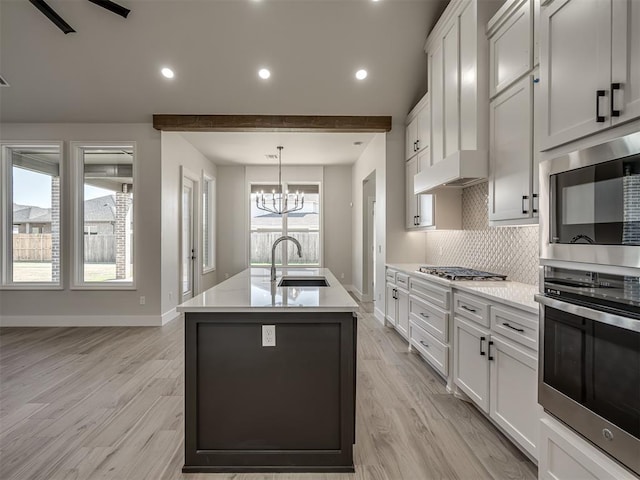 kitchen featuring sink, hanging light fixtures, stainless steel appliances, white cabinets, and a center island with sink