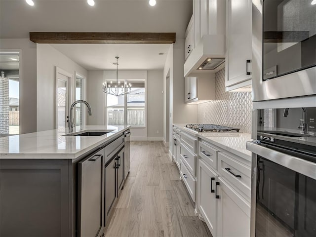 kitchen featuring sink, white cabinets, backsplash, hanging light fixtures, and a kitchen island with sink