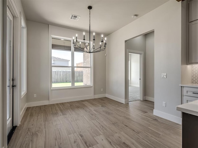 unfurnished dining area featuring an inviting chandelier and light hardwood / wood-style floors