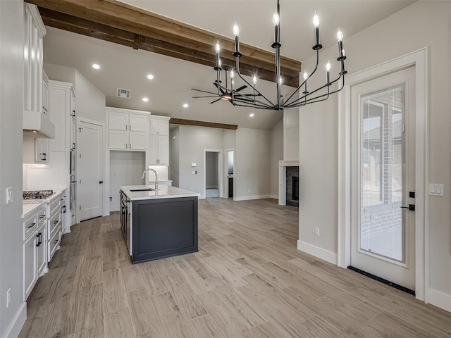 kitchen featuring appliances with stainless steel finishes, beamed ceiling, an island with sink, sink, and white cabinets