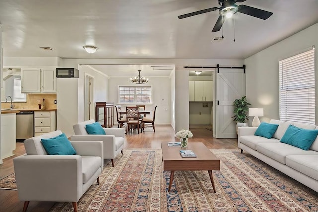 living room featuring ceiling fan with notable chandelier, a barn door, sink, and light wood-type flooring