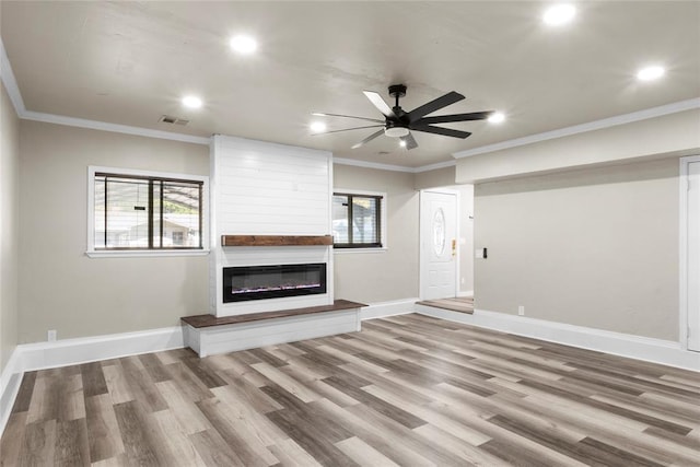 unfurnished living room featuring a fireplace, wood-type flooring, crown molding, and a healthy amount of sunlight