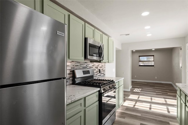 kitchen with appliances with stainless steel finishes, green cabinetry, decorative backsplash, light hardwood / wood-style flooring, and light stone counters