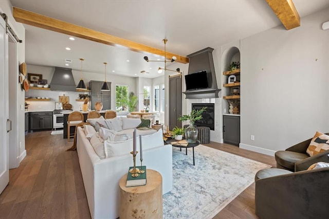 living room with beamed ceiling, a barn door, a large fireplace, built in shelves, and dark hardwood / wood-style flooring