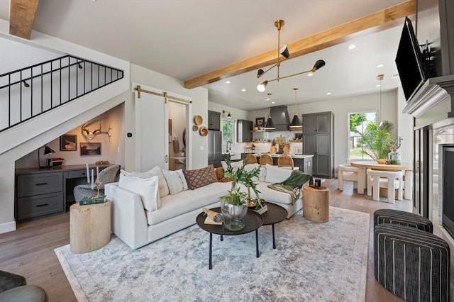 living room featuring light hardwood / wood-style flooring, beamed ceiling, and a barn door