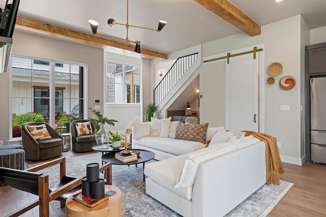 living room with beamed ceiling, a barn door, and light wood-type flooring