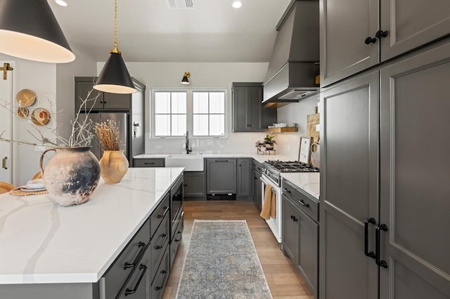 kitchen with appliances with stainless steel finishes, premium range hood, sink, pendant lighting, and gray cabinets