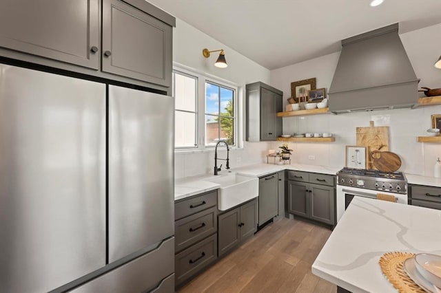 kitchen featuring stainless steel appliances, light hardwood / wood-style floors, sink, gray cabinetry, and custom range hood