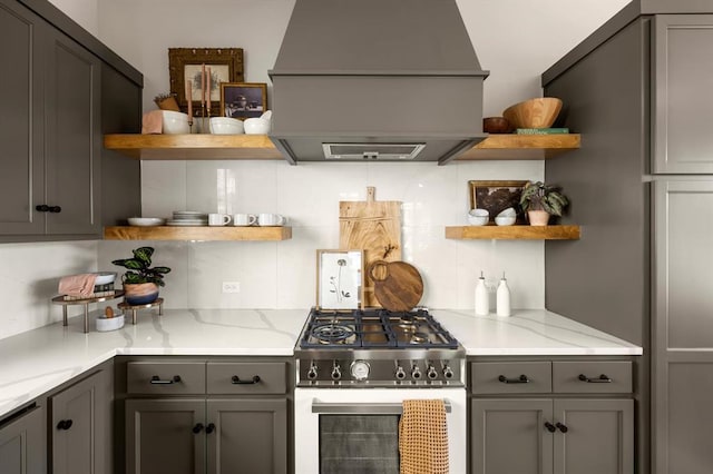 kitchen with premium range hood, high end stainless steel range oven, tasteful backsplash, and light stone counters