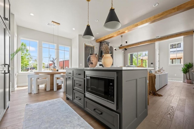 kitchen featuring hardwood / wood-style floors, a center island, hanging light fixtures, stainless steel microwave, and gray cabinetry