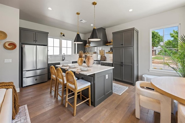 kitchen with stainless steel fridge, custom range hood, decorative light fixtures, gray cabinets, and a healthy amount of sunlight