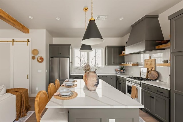 kitchen with appliances with stainless steel finishes, custom range hood, a barn door, hanging light fixtures, and gray cabinetry