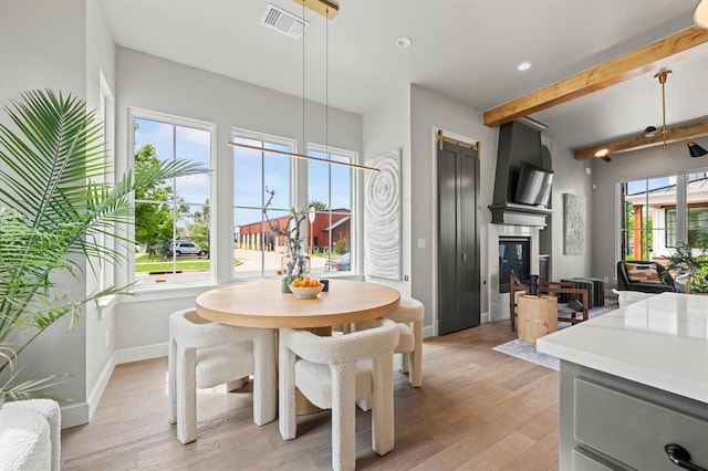 dining room with a large fireplace, light wood-type flooring, beam ceiling, and plenty of natural light