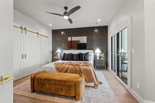 bedroom with access to outside, light wood-type flooring, ceiling fan, and a barn door