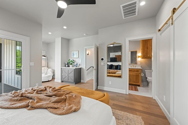 bedroom with ensuite bath, access to exterior, ceiling fan, light hardwood / wood-style flooring, and a barn door