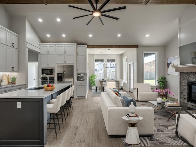 living room featuring lofted ceiling, a stone fireplace, sink, light hardwood / wood-style flooring, and ceiling fan with notable chandelier