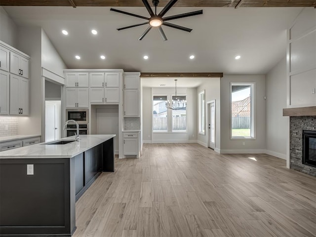 kitchen featuring a stone fireplace, built in microwave, lofted ceiling, sink, and a kitchen island with sink