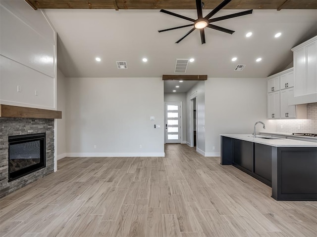 kitchen with lofted ceiling, sink, white cabinetry, a fireplace, and decorative backsplash