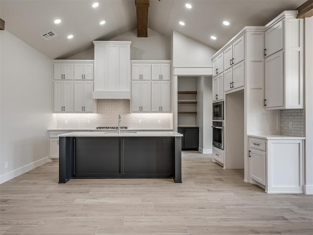 kitchen with white cabinetry, vaulted ceiling with beams, an island with sink, built in microwave, and oven