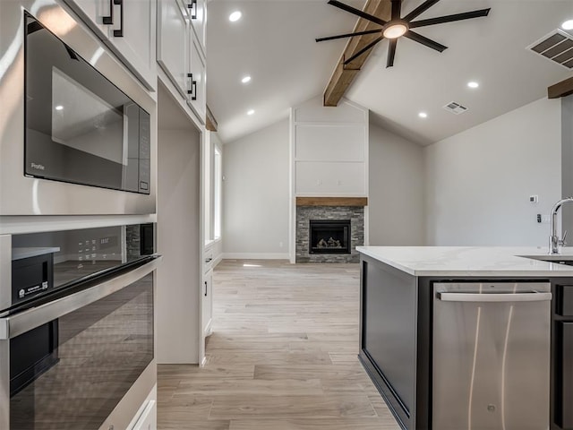 kitchen with vaulted ceiling with beams, a stone fireplace, stainless steel appliances, and white cabinets