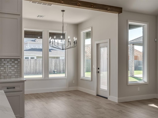 unfurnished dining area featuring an inviting chandelier, beam ceiling, and light wood-type flooring