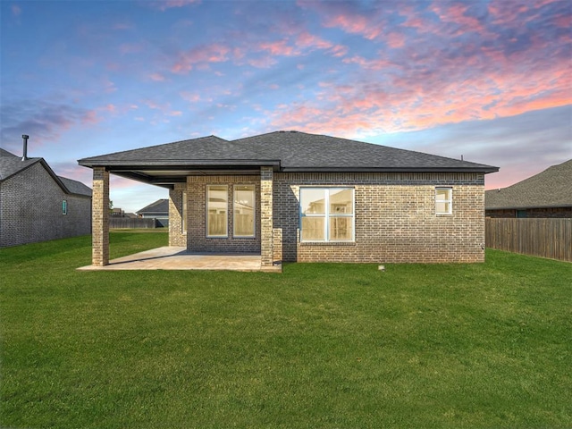 back house at dusk with a patio and a lawn