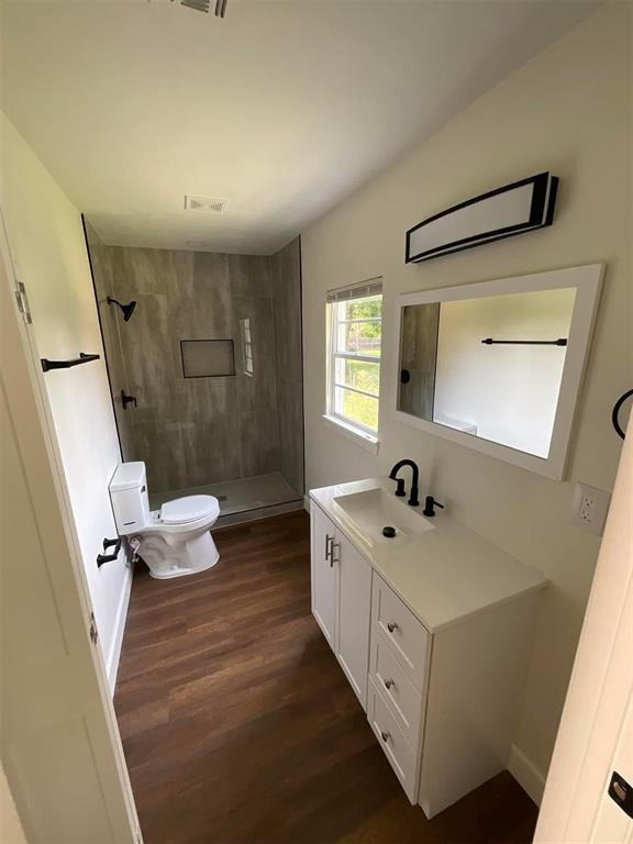 bathroom with vanity, hardwood / wood-style flooring, toilet, and tiled shower