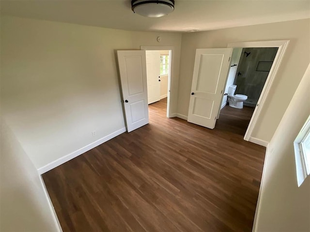 unfurnished bedroom with ensuite bathroom and dark hardwood / wood-style flooring