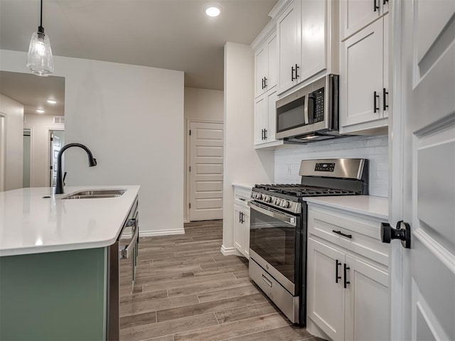 kitchen featuring sink, light hardwood / wood-style flooring, hanging light fixtures, appliances with stainless steel finishes, and white cabinets