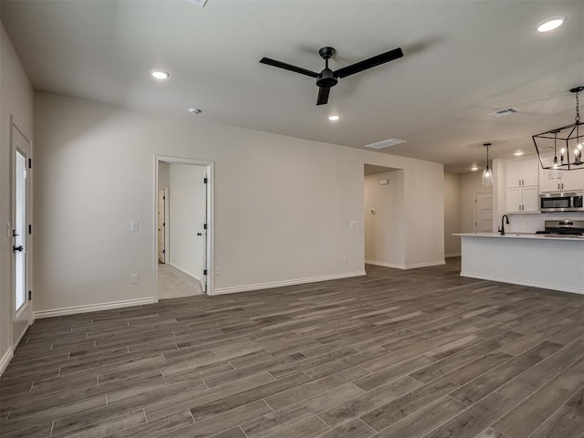 unfurnished living room with sink, ceiling fan with notable chandelier, and dark hardwood / wood-style floors