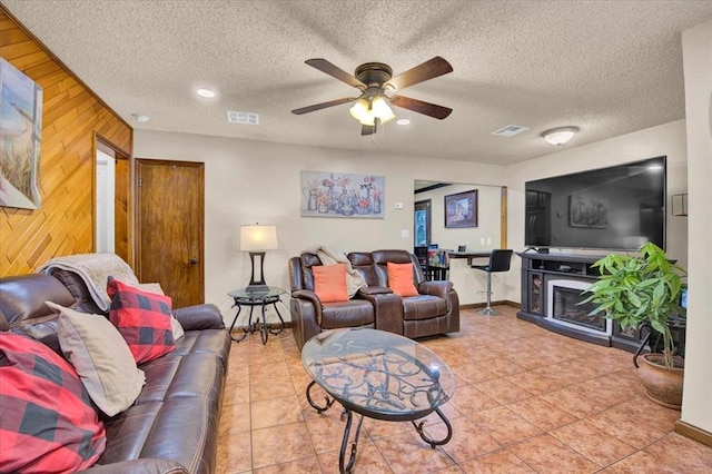 living room featuring ceiling fan, tile patterned flooring, a textured ceiling, and wooden walls