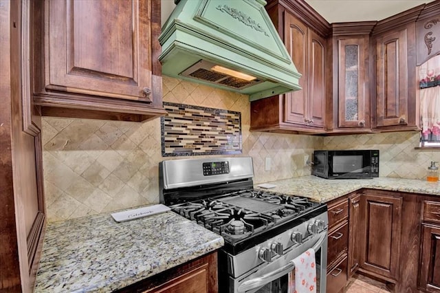 kitchen with premium range hood, backsplash, gas stove, and light stone countertops