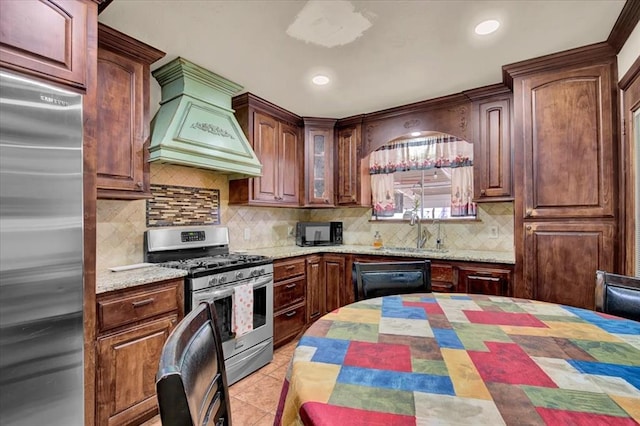 kitchen featuring black appliances, premium range hood, sink, backsplash, and light stone counters