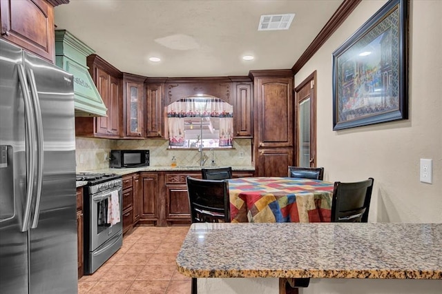 kitchen featuring light tile patterned floors, light stone countertops, ornamental molding, decorative backsplash, and stainless steel appliances