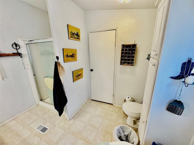 bathroom with a textured ceiling, toilet, and a shower with door