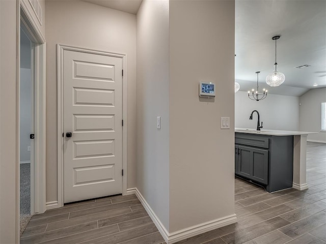hall featuring wood finish floors, a chandelier, a sink, and baseboards