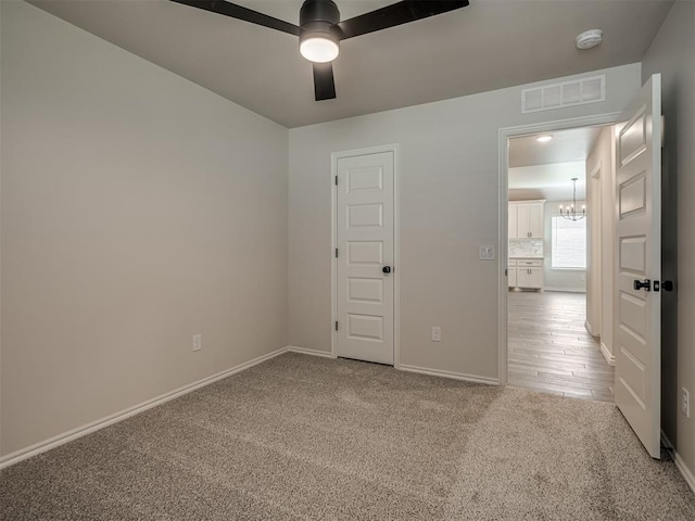 unfurnished room with baseboards, ceiling fan with notable chandelier, visible vents, and carpet