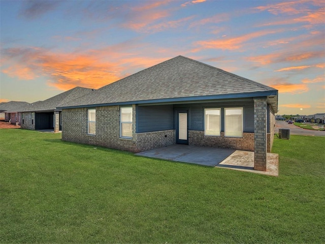rear view of property featuring a shingled roof, a yard, central air condition unit, a patio, and brick siding