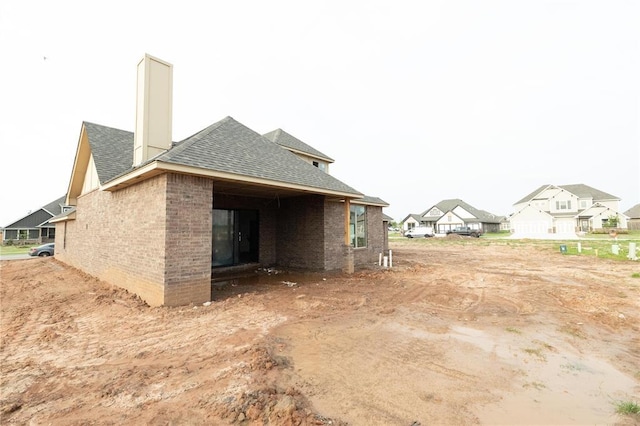 view of home's exterior featuring roof with shingles, a chimney, brick siding, and a residential view