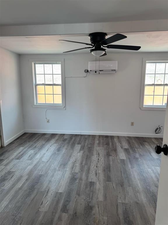 unfurnished room with dark wood-type flooring, an AC wall unit, and ceiling fan