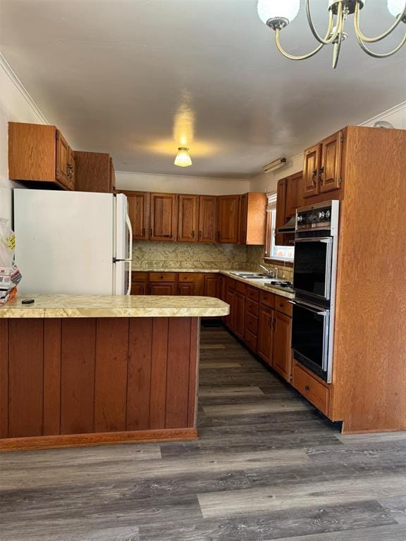 kitchen featuring dark wood-type flooring, crown molding, a chandelier, white refrigerator, and black double oven