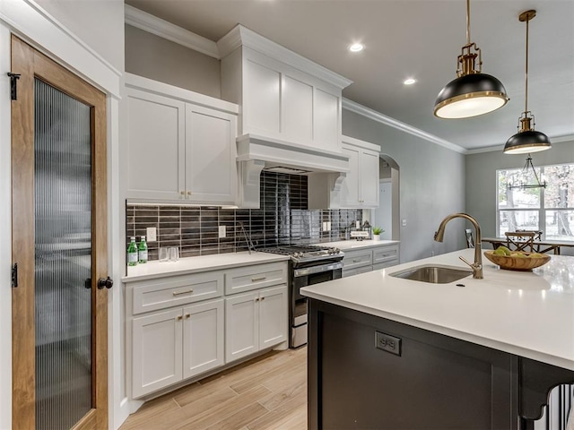 kitchen featuring custom exhaust hood, sink, decorative light fixtures, white cabinetry, and stainless steel gas range oven