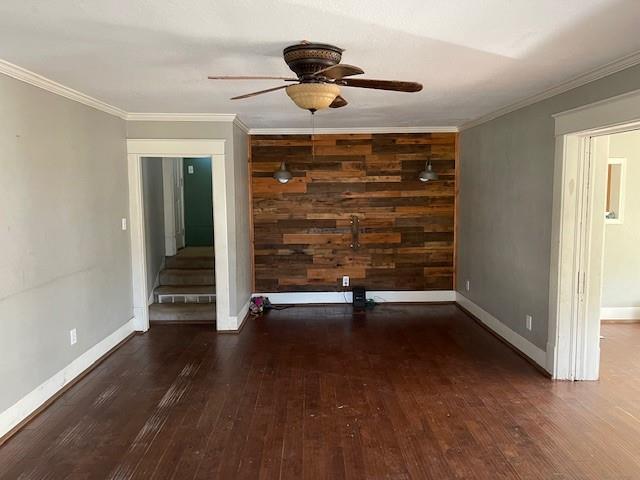 empty room featuring crown molding, wood walls, ceiling fan, and dark hardwood / wood-style flooring