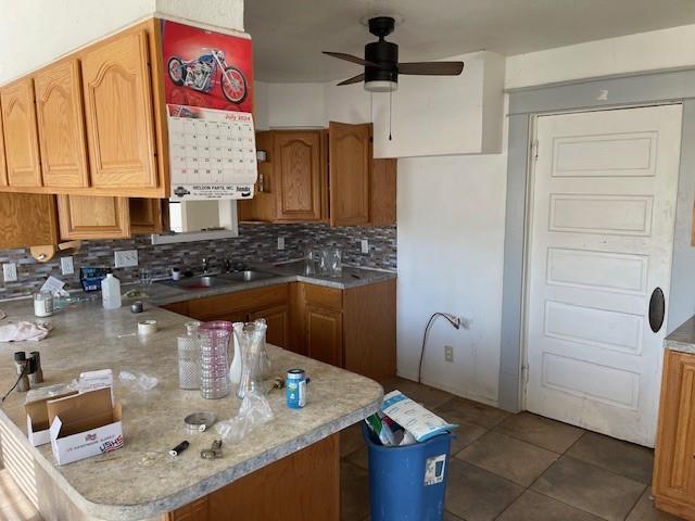 kitchen featuring kitchen peninsula, ceiling fan, sink, dark tile patterned flooring, and decorative backsplash